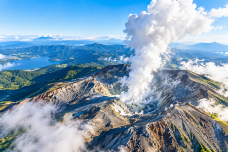 「山岳地帯の火口から白い噴煙が立ち上る雄大な火山風景を上空から捉えた映像」