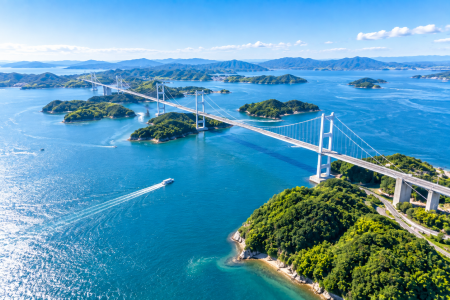 「青い海に浮かぶ緑豊かな島々と長い吊り橋を上空から捉えた、しまなみ海道の美しい空撮風景」