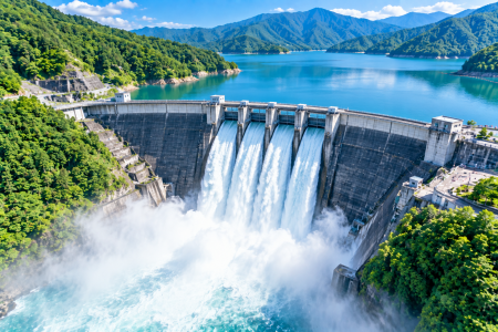 「青い湖を望む山間のダムから豪快に放水され、白い水しぶきと水煙が広がる迫力ある空撮風景」